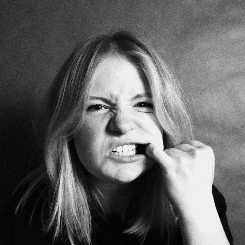 Woman with clenched teeth and her finger in her mouth