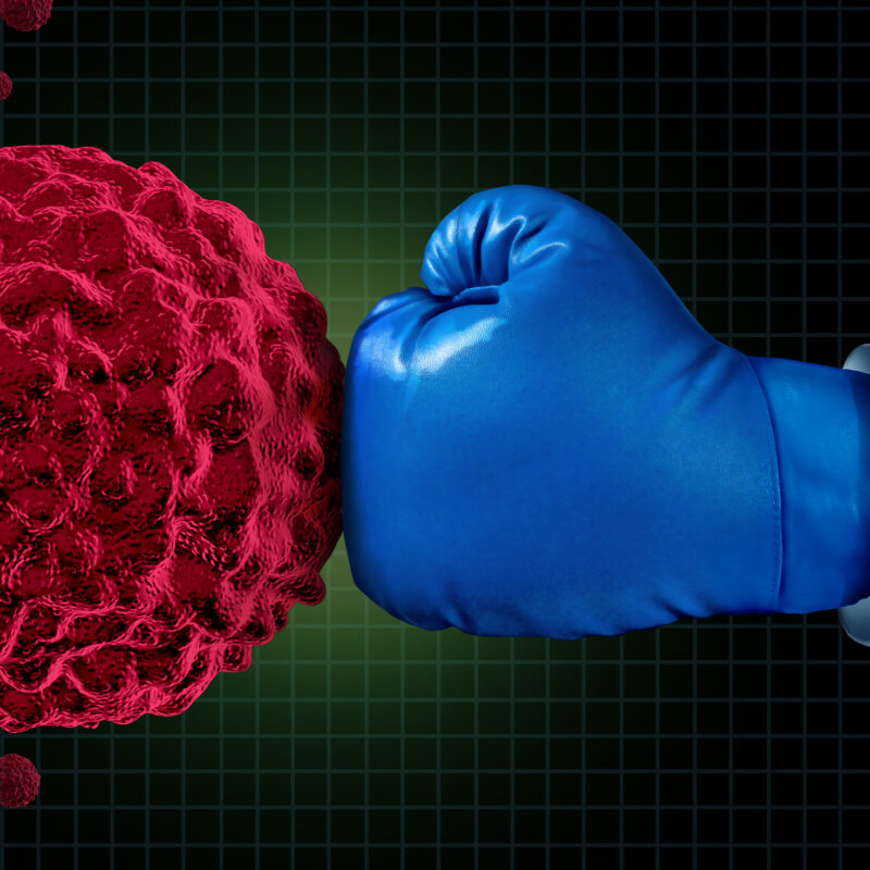 Cancer fight medical concept with an arm of a doctor wearing a blue boxing glove fighting a group of malignant human cells as a health care metaphor for researching a cure for dangerous tumors and therapy to remove illness.
