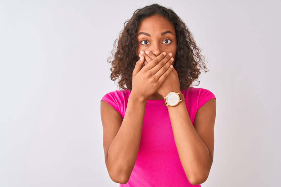 woman in pink shirt covering her mouth because of dental emergency