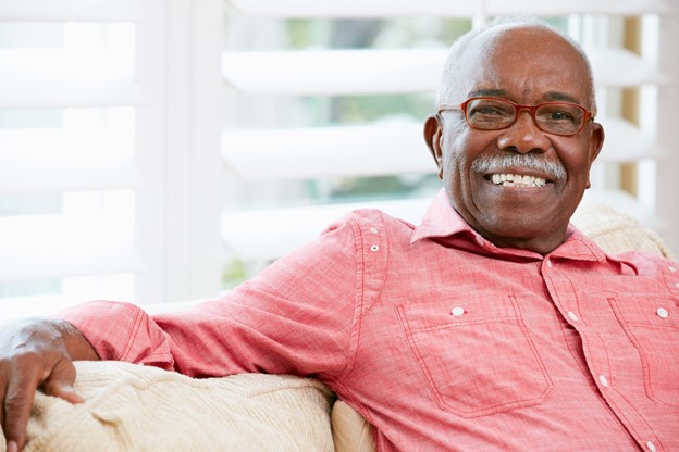 older black man smiling, wearing red shirt on couch