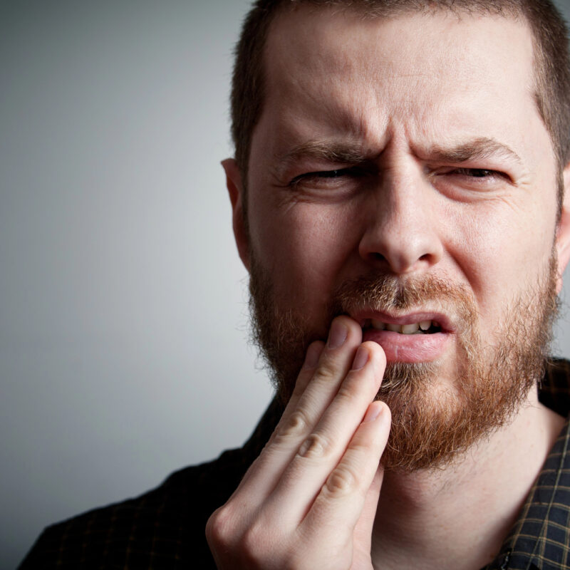 man with toothache, hand on jaw and frowning