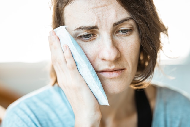 woman holding an ice pack to her face because of mouth pain