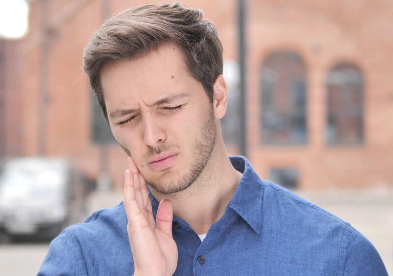 man experiencing tooth pain while walking outside