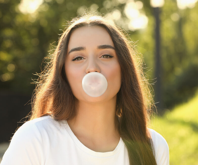 Beautiful young woman blowing bubble gum in park