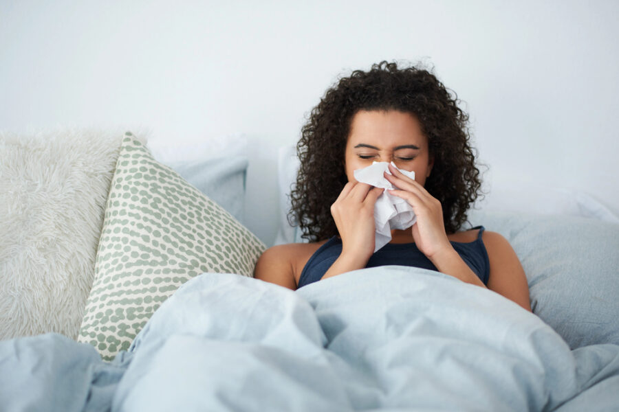 black woman sitting in bed blowing her nose