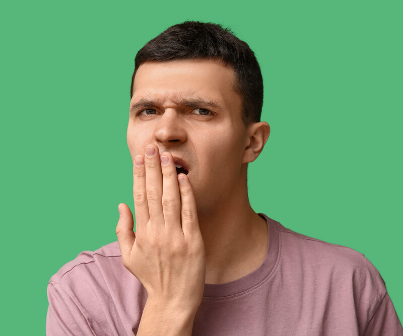 Handsome young man feeling bad smell from mouth on green background