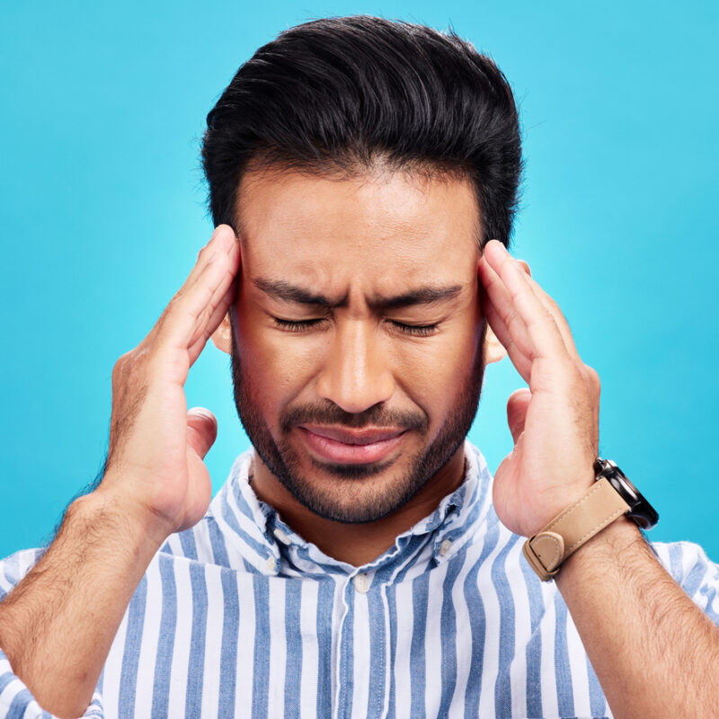 Man with headache, pain and stress with anxiety and mental health problem or crisis isolated on blue background. Male person hands holding head, massage temple with depression and migraine in studio
