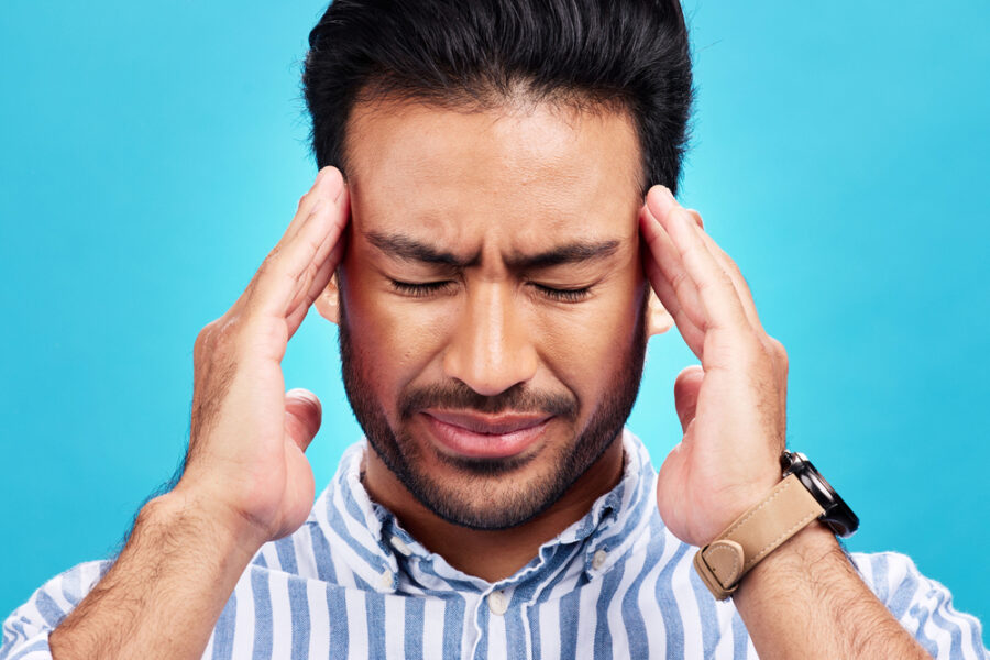Man with headache, pain and stress with anxiety and mental health problem or crisis isolated on blue background. Male person hands holding head, massage temple with depression and migraine in studio