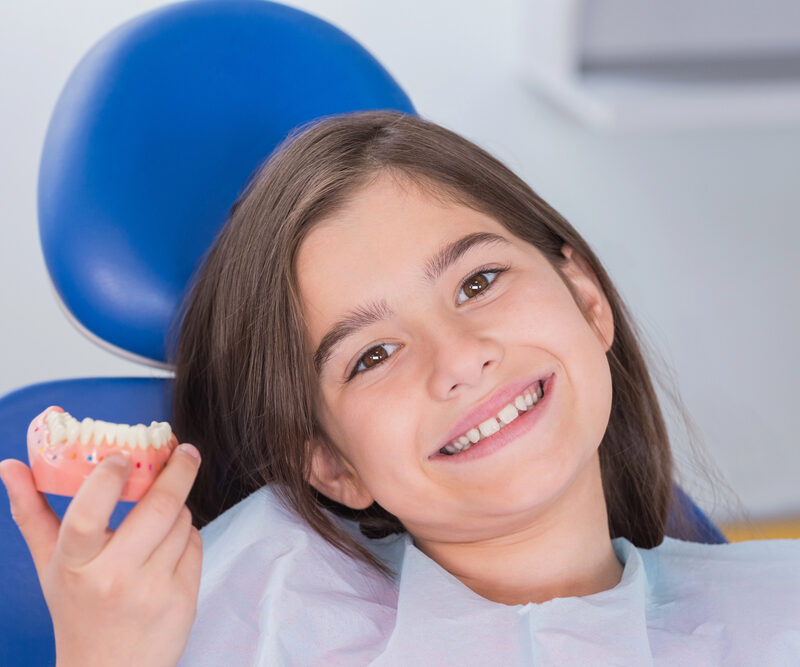 young girl sitting in dental chair holding model of bottom jaw