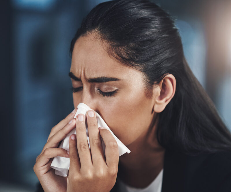 Woman, influenza and blowing nose in office with tissue, flu or cold as accountant in finance agency. Female person, sick and unhealthy with sneeze, hay fever or sinus infection with allergy or virus.