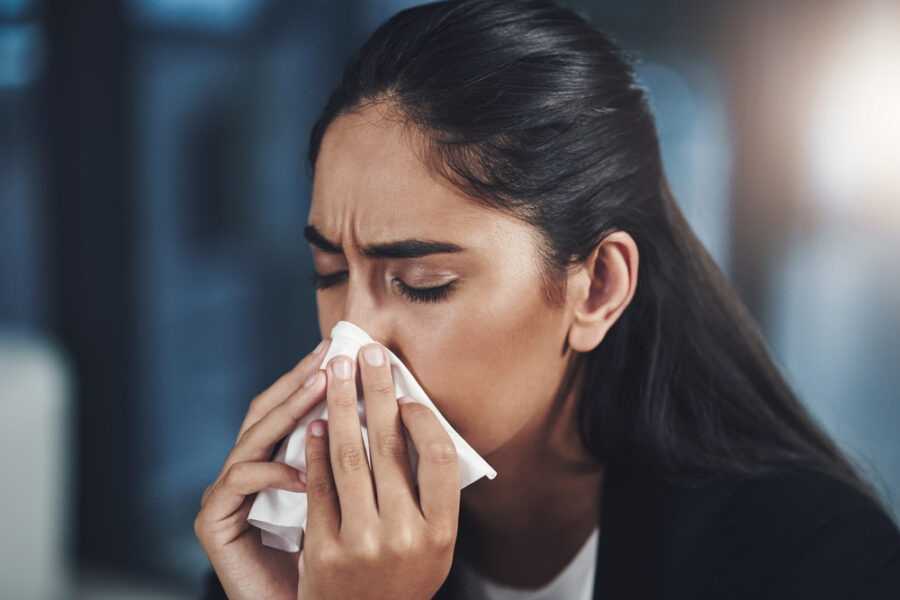 Woman, influenza and blowing nose in office with tissue, flu or cold as accountant in finance agency. Female person, sick and unhealthy with sneeze, hay fever or sinus infection with allergy or virus.