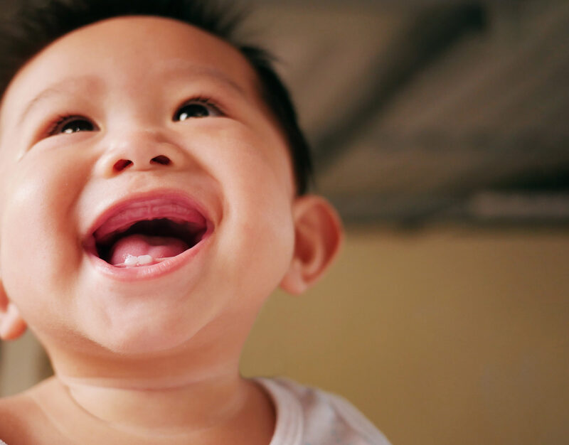 Asian baby smiling with two rises baby milk teeth.