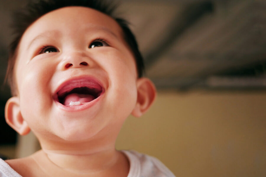 Asian baby smiling with two rises baby milk teeth.